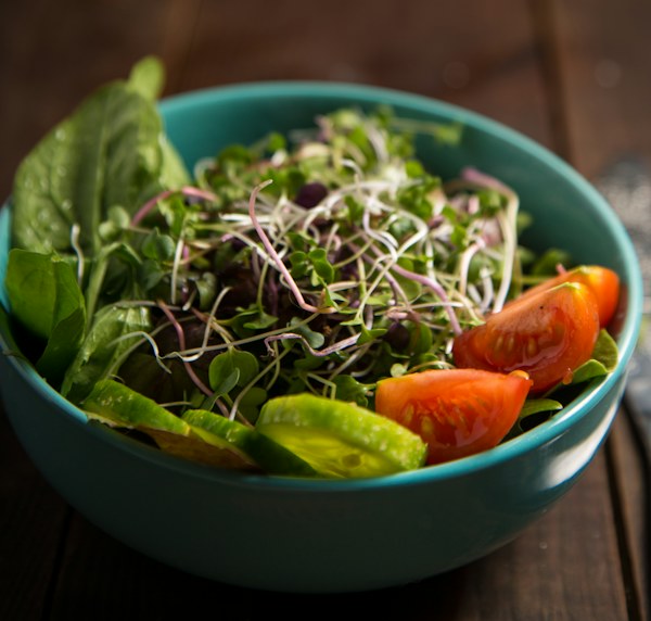 Ensalada de hojas verdes, brotes y tomates en un cuenco turquesa
